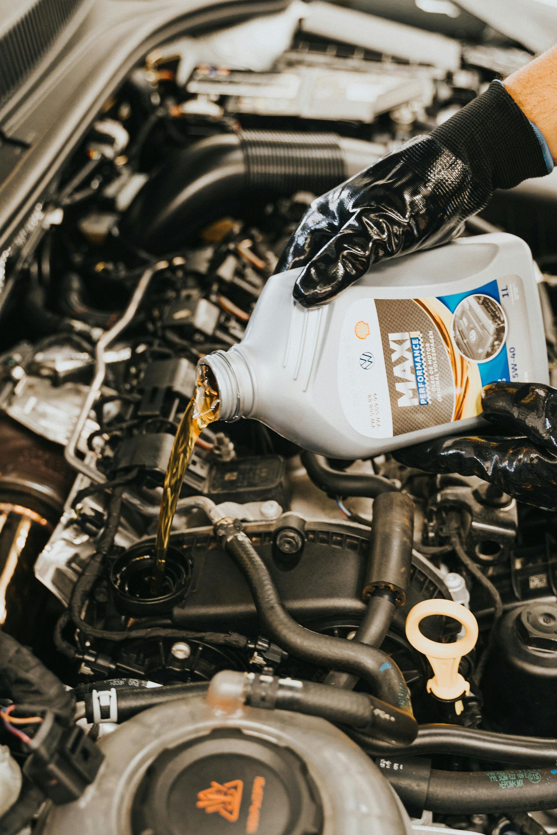 A gloved hand pouring oil into a car engine during an oil change.