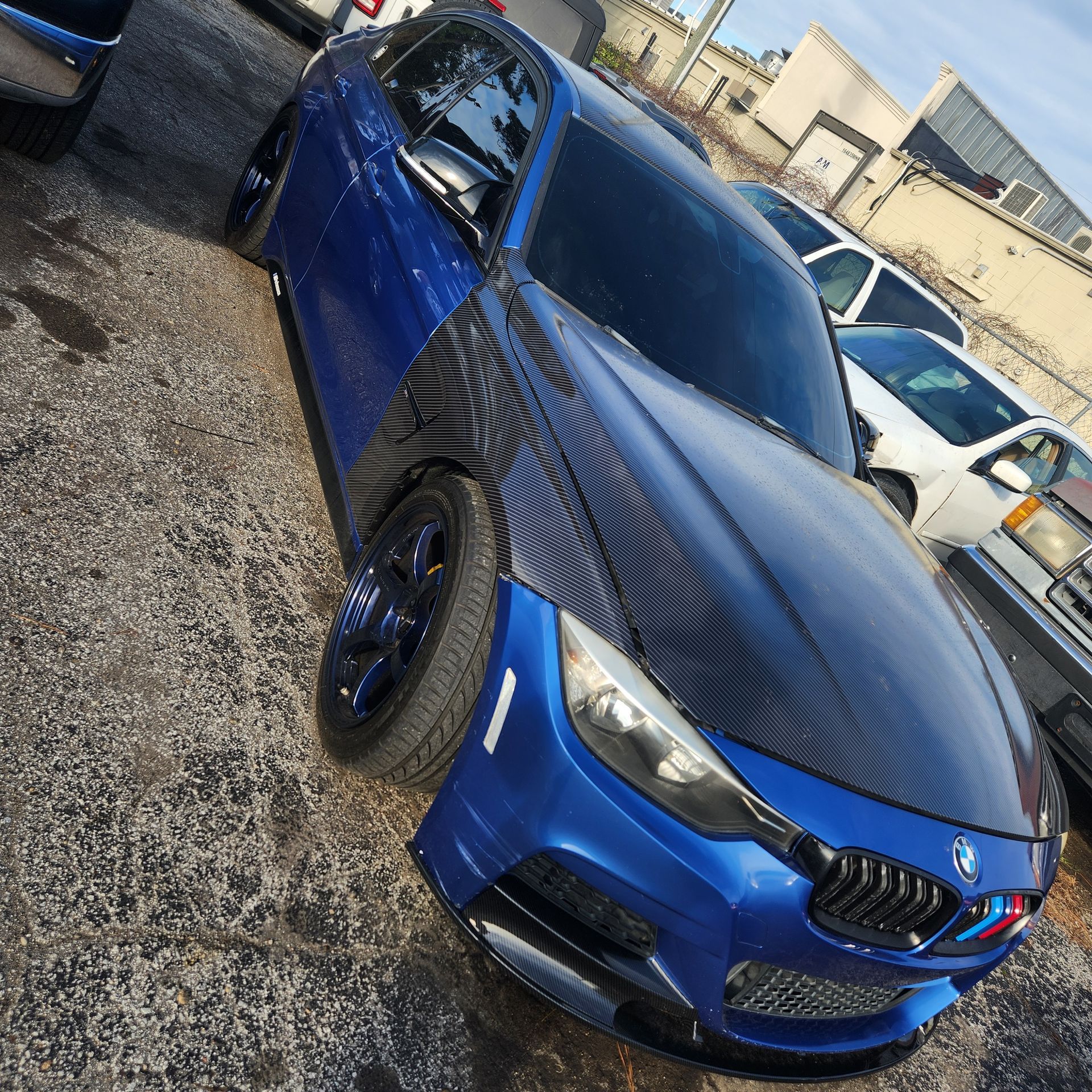 Blue BMW sports car with carbon fiber hood parked on a lot.