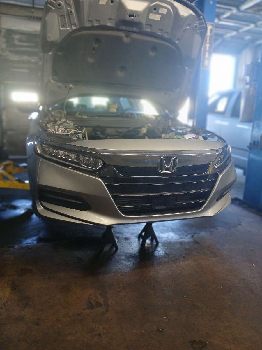 Silver Honda Accord with its hood open, jack stands supporting the car in a garage.