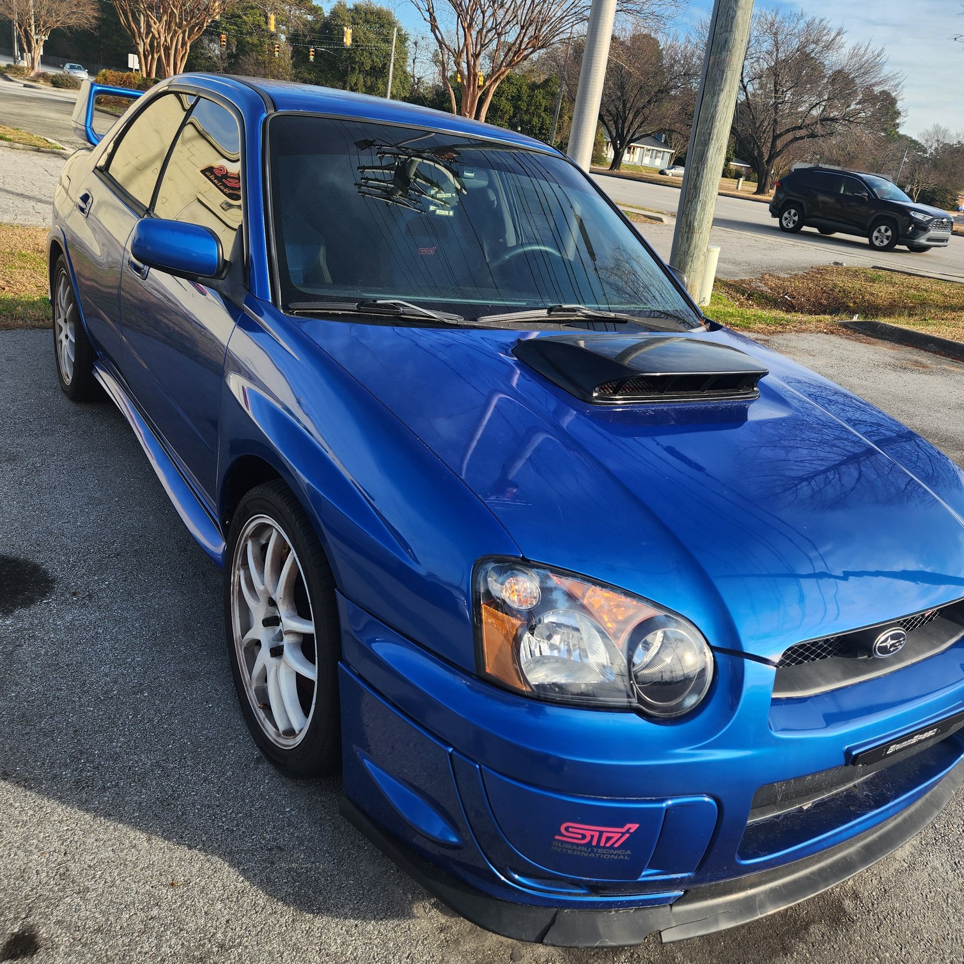 Blue Subaru Impreza WRX STI with a black hood scoop parked on pavement in an outdoor setting.