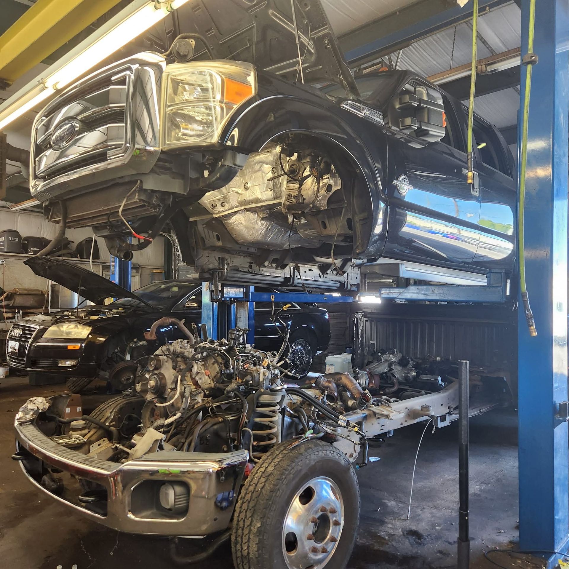 Black truck on a lift in a repair shop, partially disassembled with engine exposed.