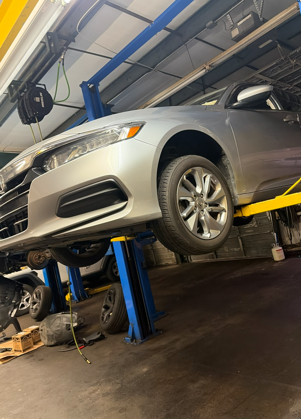 Silver car raised on a blue and yellow lift inside a garage.