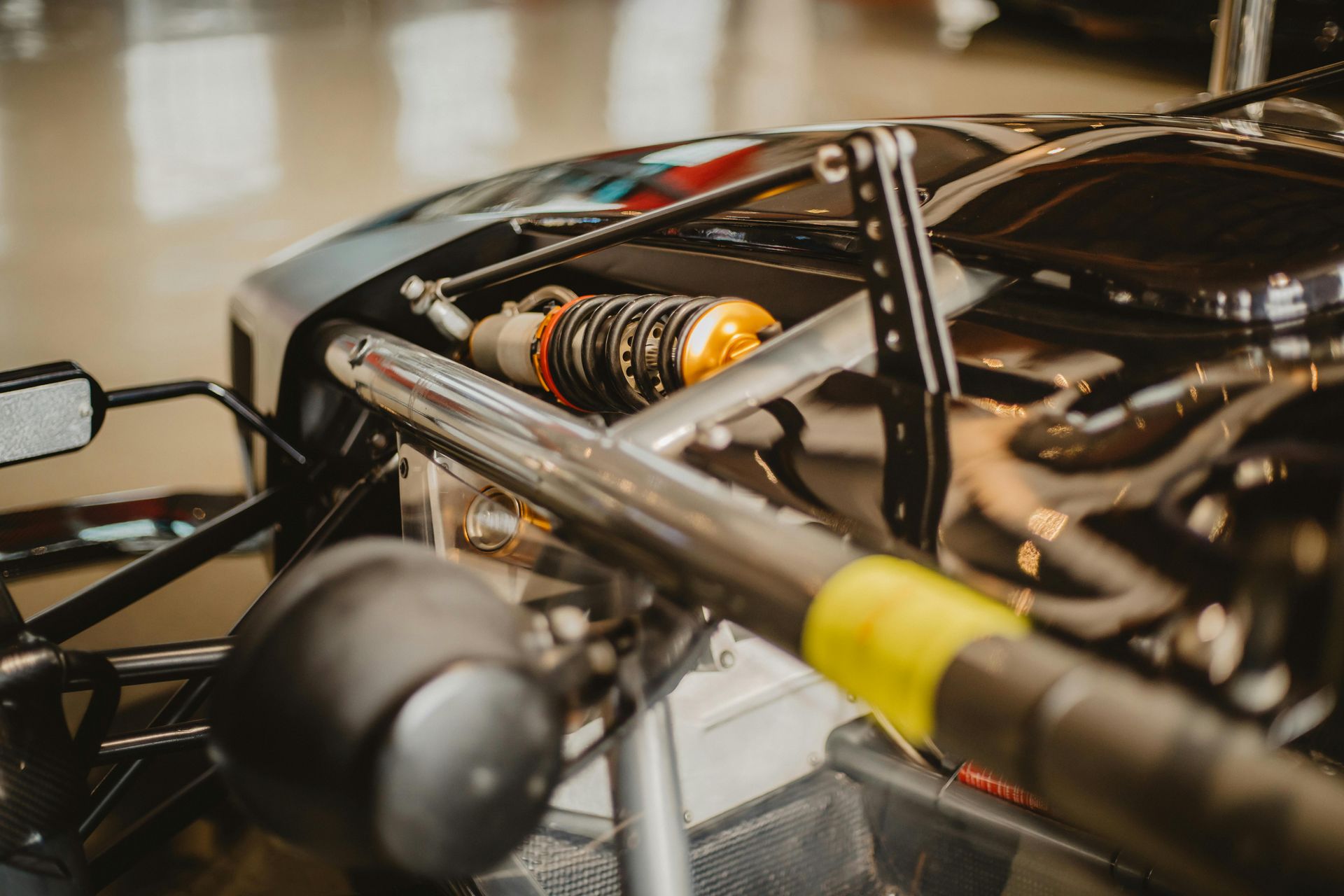 Close-up of a black race car's suspension and shock absorber, featuring orange and silver parts.
