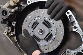 Hands in black gloves installing a clutch disc in a car's transmission.